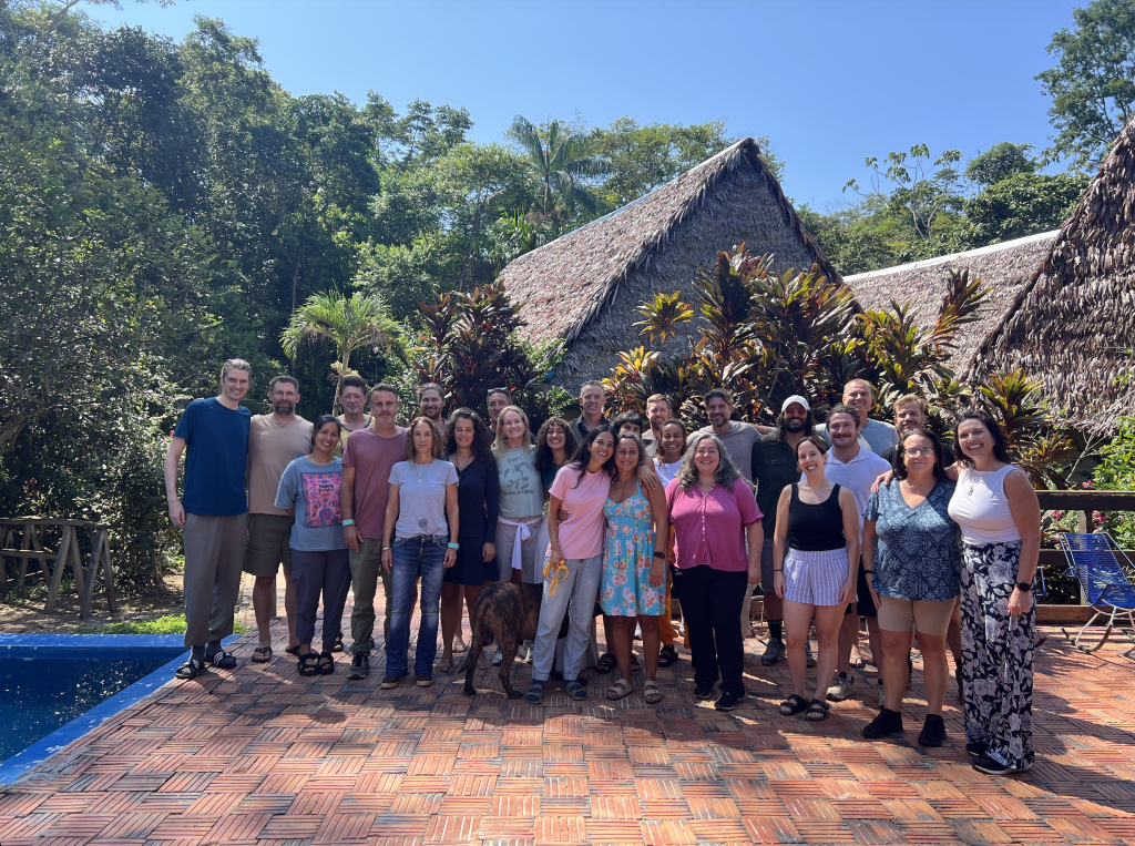 Blue Morpho retreat group gathered beside the pool with thatched jungle lodges behind them