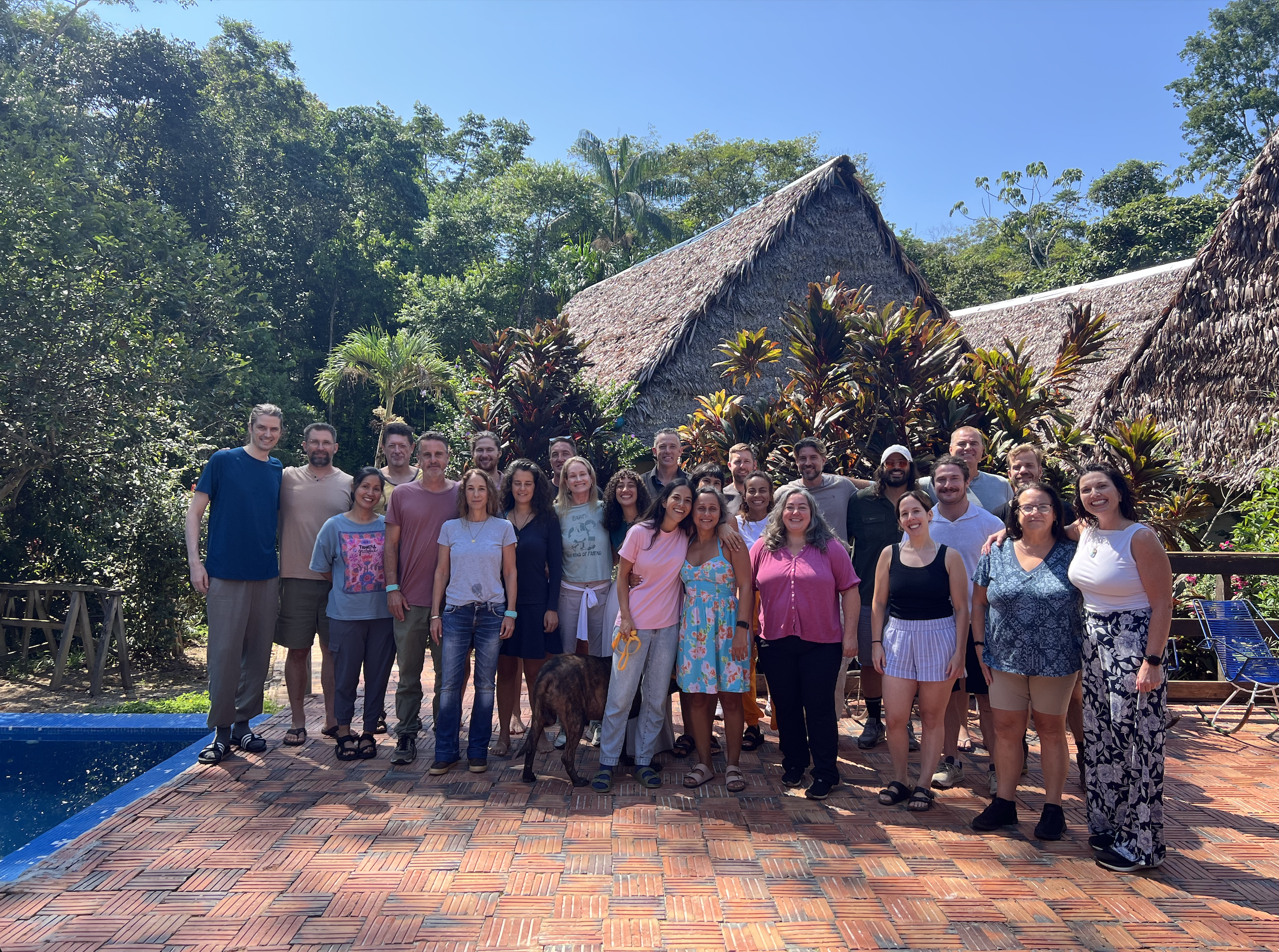 Blue Morpho retreat group gathered beside the pool with thatched jungle lodges behind them