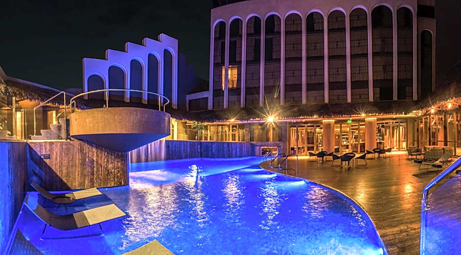DoubleTree Iquitos Pool at Night - Abby Kojola In Peru DoubleTree Iquitos pool lit blue at night with a waterfall spilling from the elevated hot tub